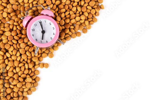 A frame made of dry cat (dog) food and a pink alarm clock on a white isolated background. Space for text. Balanced nutrition. Morning time to feed pets. Template for the design.