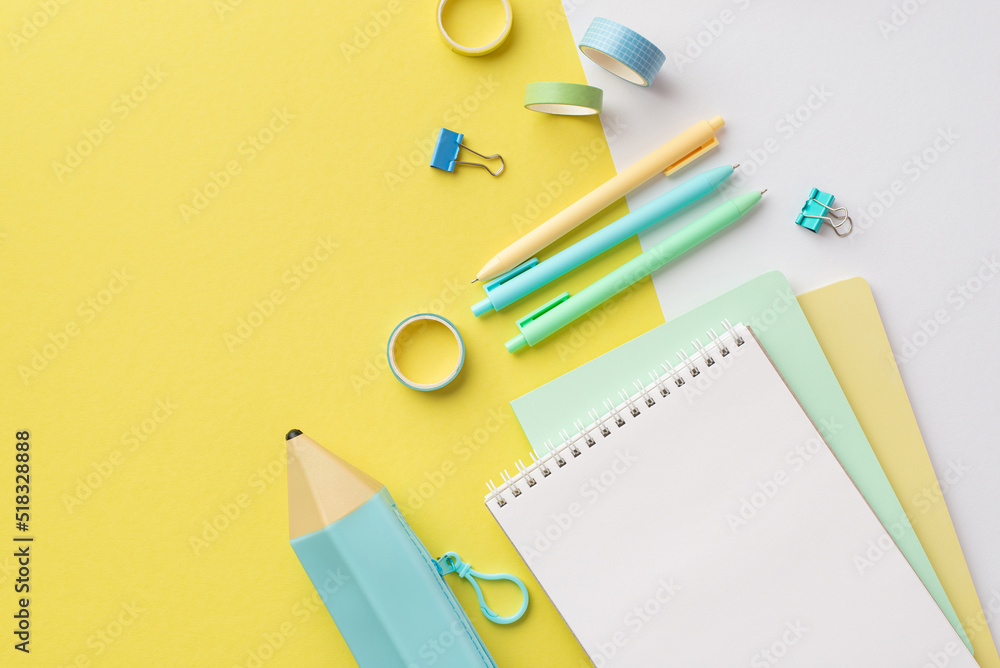 School accessories concept. Top view photo of blue pencil-case stack of copybooks colorful pens binder clips and adhesive tape on bicolor yellow and white background School accessories concept. Top view photo of blue pencil-case stack of copybooks colorful pens binder clips and adhesive tape on bicolor yellow and white background