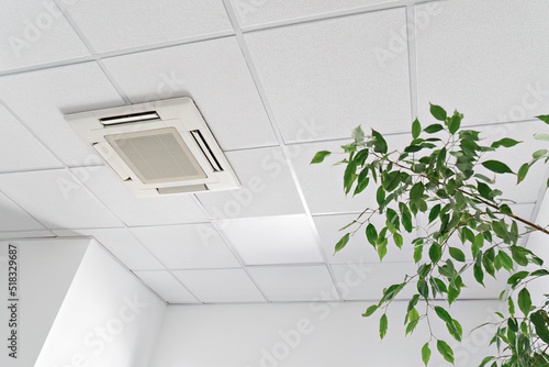 Cassette air conditioner on ceiling in modern light office or apartment with green ficus plant leaves. Indoor air quality and clean filters concept