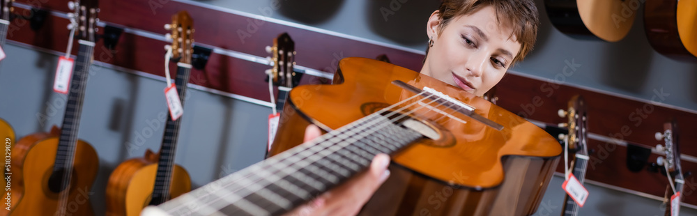 Musician looking at blurred acoustic guitar in music store, banner. Musician looking at blurred acoustic guitar in music store, banner.
