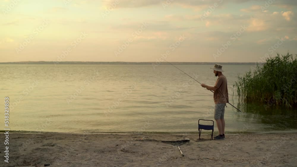 caucasian bearded man fishes in the evening at sunset on a summer day on a river in the countryside, collects a fishing rod and finishes the process of catching fish. caucasian bearded man fishes in the evening at sunset on a summer day on a river in the countryside, collects a fishing rod and finishes the process of catching fish.