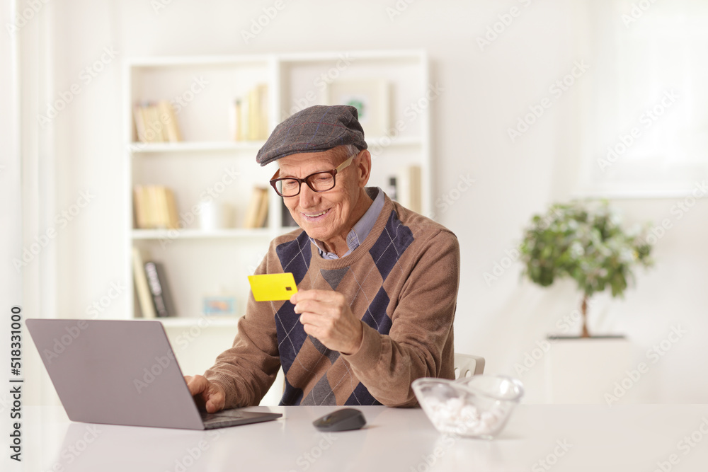 Cheerful elderly man paying with a credit card on a laptop computer Cheerful elderly man paying with a credit card on a laptop computer