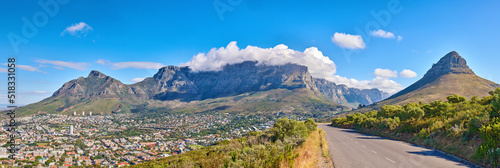 Table Mountain is a hiking destination for tourists and locals surrounded by nature, trees and houses. Scenic road view of clouds resting on the popular tourist attraction in the city Cape Town.