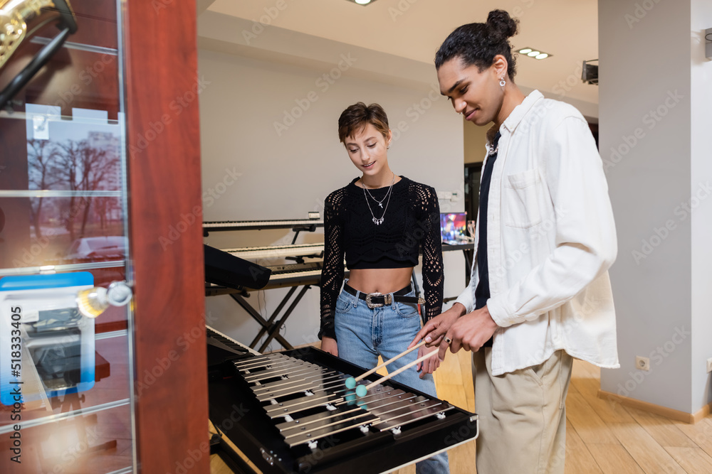 African american seller playing xylophone near customer in music store. African american seller playing xylophone near customer in music store.