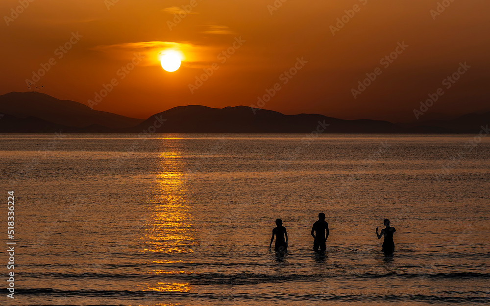 Three friends near the sea beach with colorful sunset sky. Panoramic beach landscape. Tropical beach and seascape and a distant island in the background. Golden sunset sky, tranquil summer mood. Three friends near the sea beach with colorful sunset sky. Panoramic beach landscape. Tropical beach and seascape and a distant island in the background. Golden sunset sky, tranquil summer mood.