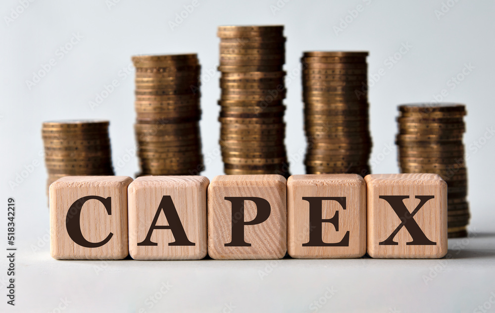 CAPEX - acronym on wooden cubes on the background of stacks of coins - obrazy, fototapety, plakaty 