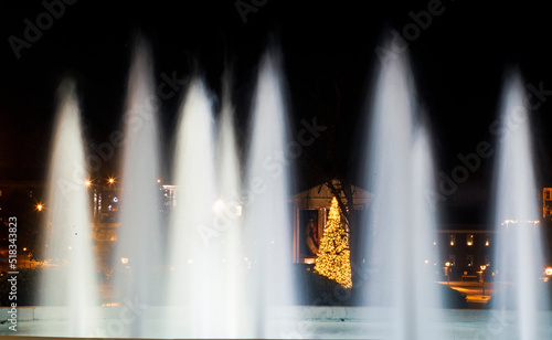 A fountain streams water in front a Christmas tree. 