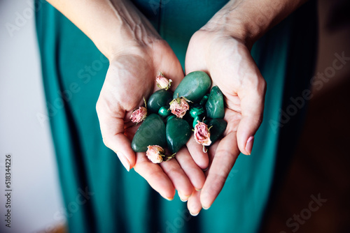 A woman holds in her hands several malachite stones with several dry pink roses. She is wearing a pretty emerald green dress.. photo