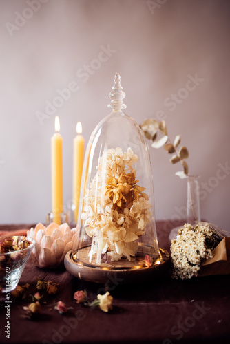 Beautiful still life with an urn filled with dried flowers, a bowl filled with small dried roses, several lighted candles and a figure in the shape of a lotus flower..