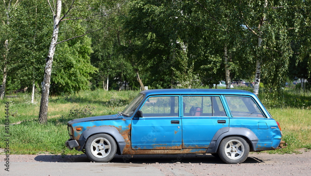 An old blue rusty Soviet car is parked on the street, Badaeva Street, St. Petersburg, Russia, July 2022