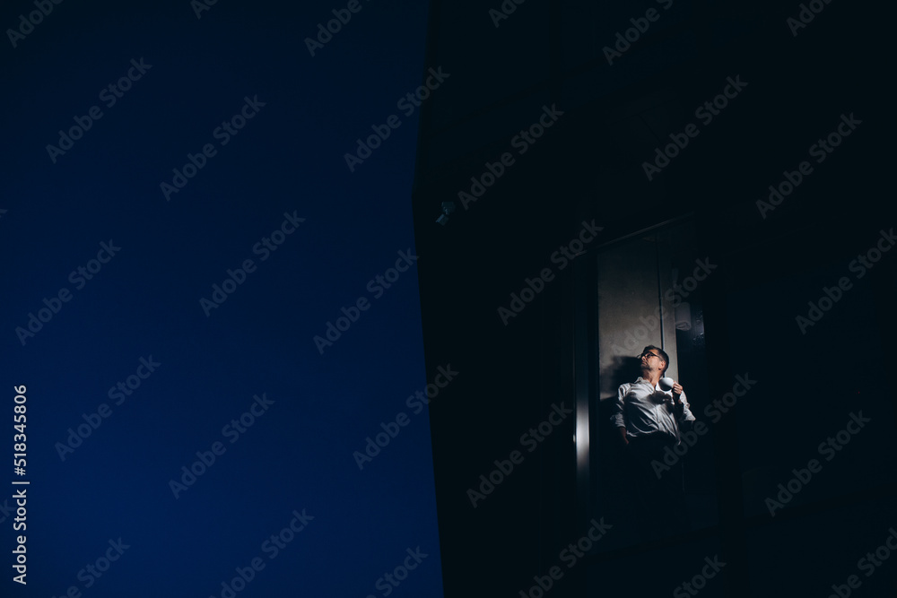 Fototapeta premium Senior manager is alone in the office at night, drinking coffee and looking out the window.