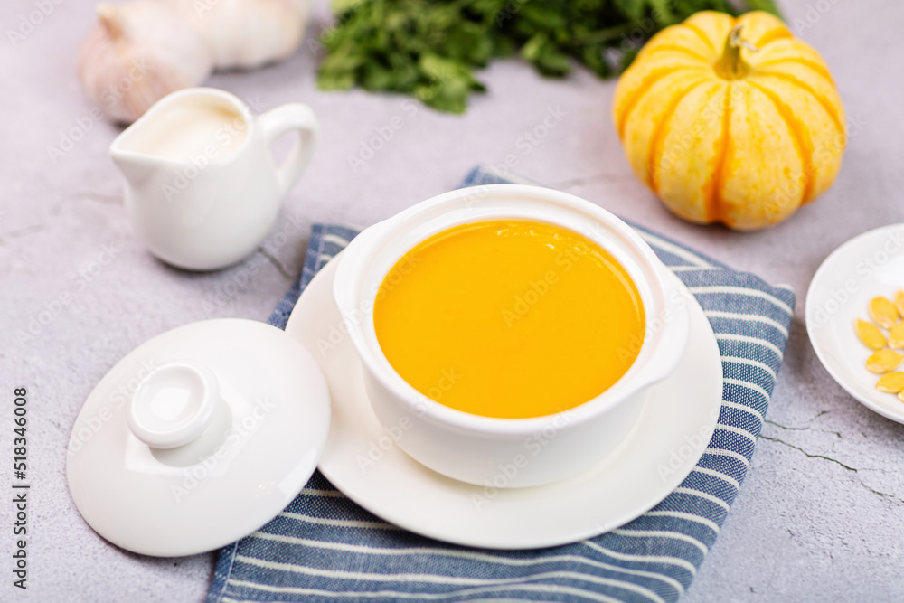 Flat lay of Pumpkin Cream soup served with seeds on gray concrete background. Top view of Autumn cream-soup in country style and fallen autumn maple leaves. Useful dietary snack and lunch Flat lay of Pumpkin Cream soup served with seeds on gray concrete background. Top view of Autumn cream-soup in country style and fallen autumn maple leaves. Useful dietary snack and lunch