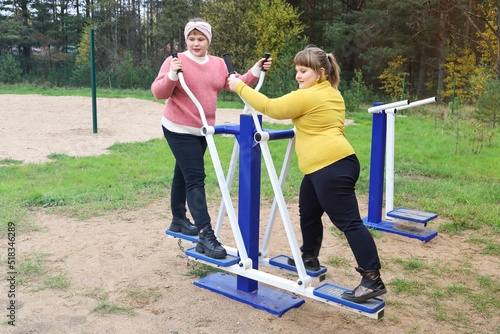 Two chubby girls performs sports exercises on street simulators