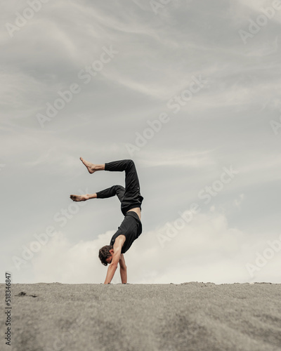 Young man stands on hands on the sand in desert