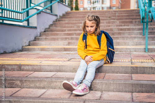 Back to elementary, primary school. Little sad unhappy girl with backpack. Lonely schoolgirl with emotional problems, victim of bullying in schoolyard. Teen in depresiion sitting alone on stair steps © velirina