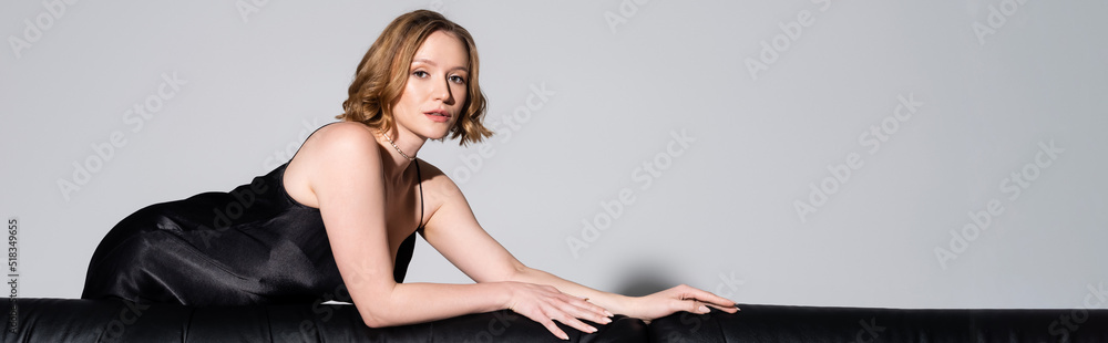sexy woman in black dress looking at camera while posing isolated on grey, banner. sexy woman in black dress looking at camera while posing isolated on grey, banner.