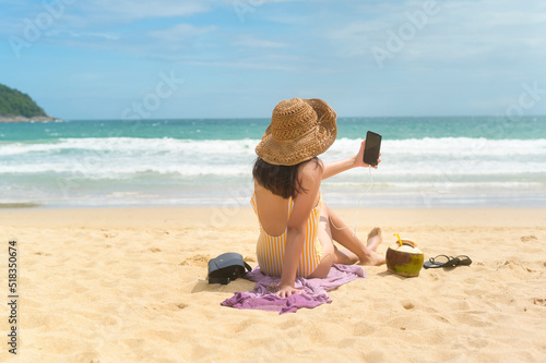 Young Beautiful woman in Bikini listening to music and using smartphone on the beach, Summer, vacation, holidays, Lifestyles concept.