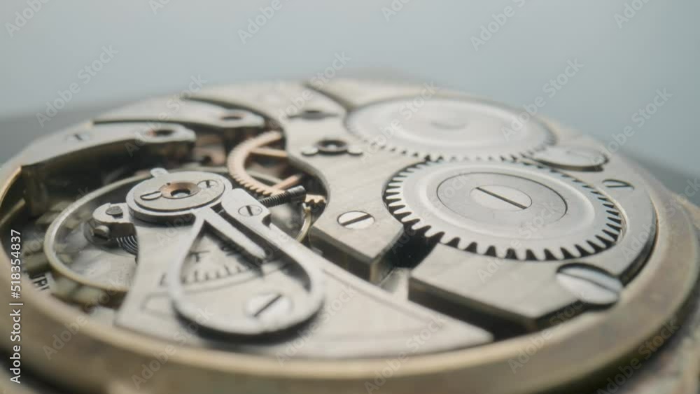 Macro shot of the internal parts of antique pocket watch turning on light gray background. Clockwork with rotating spring, gears, cogwheel and tootheds wheels. Disassembled silver retro watch inside. Macro shot of the internal parts of antique pocket watch turning on light gray background. Clockwork with rotating spring, gears, cogwheel and tootheds wheels. Disassembled silver retro watch inside.