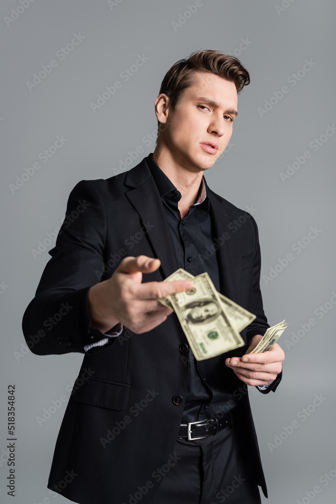 confident man in formal wear showing blurred dollars at camera isolated on grey. confident man in formal wear showing blurred dollars at camera isolated on grey.