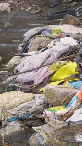 CLOSE UP: Pile of garbage waste caught between the rocks in the middle of river. River debris and plastic rubbish mix stucked on the river stones. Urgent need for waste management and eco education. photo