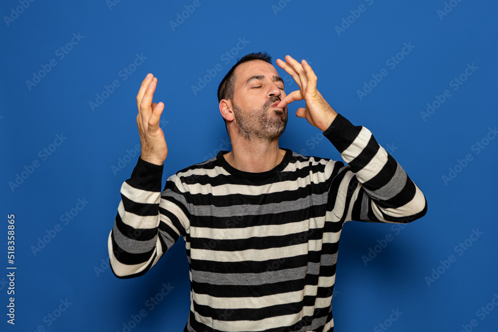 Happy business man licking fingers isolated on trendy blue studio background. Beautiful male half-length portrait. Young satisfy man. Human emotions, facial expression concept. Front view. Happy business man licking fingers isolated on trendy blue studio background. Beautiful male half-length portrait. Young satisfy man. Human emotions, facial expression concept. Front view.