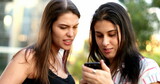 Candid young women looking at smartphone screen. Girlfriends checking cellphone frowning