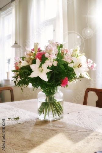 Vibrant bunch of blossoms displayed for interior decoration. Colorful bouquet in a vase on a table at home with lens flare. Fresh peruvian and easter lily flowers blooming with green foliage. © SteenoWac/peopleimages.com