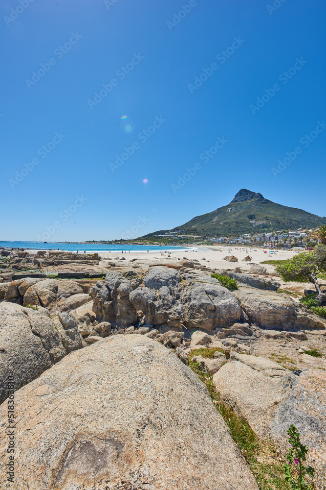 Vibrant beach near rocky shore and mountains on blue sky background with copy space. Bright summer with tourists tanning under the sun and enjoying the stunning view of Lions Head mountain, Cape Town