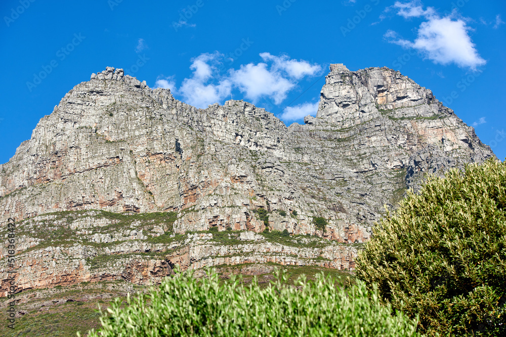 Below view of majestic mountains with bushes growing below and cloudy blue sky copy space above. Nature landscape of mountain rock outcrops with wild green plants during a bright and beautiful day