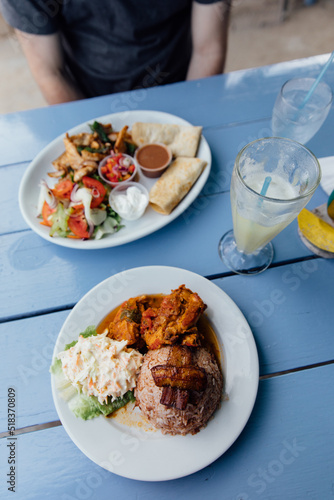 Chicken, rice, plantains, and more on two plates on a blue table