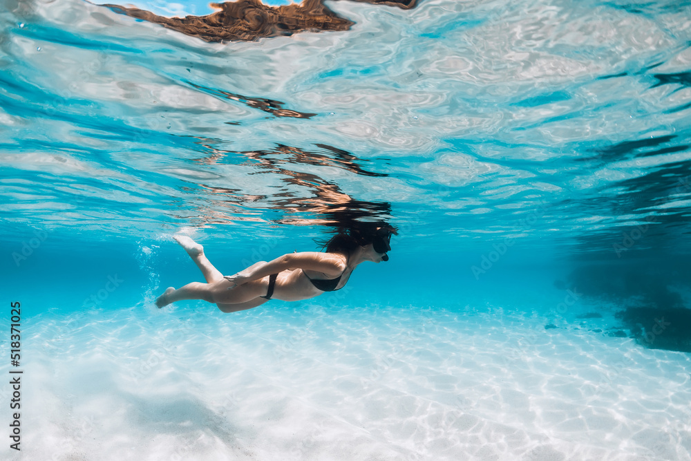 Woman in bikini and with diving mask swimming underwater in tropical ocean with white sand bottom