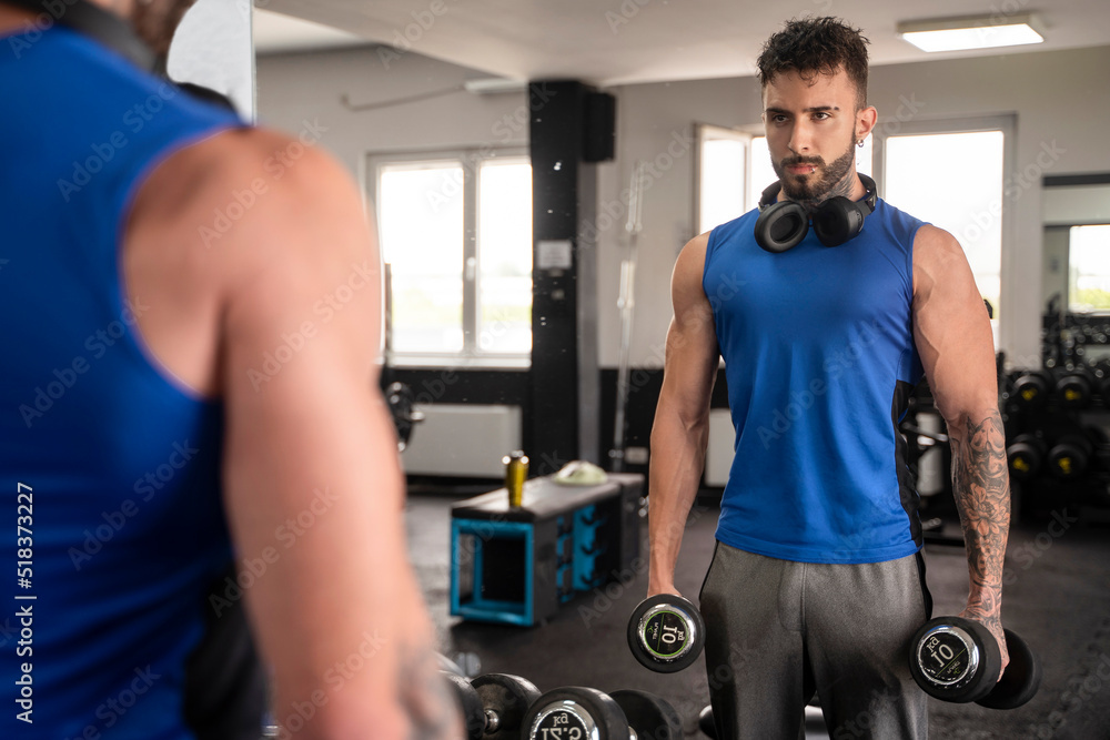 Handsome male with tattoos in his 20s training in the gym with mirror Handsome male with tattoos in his 20s training in the gym with mirror