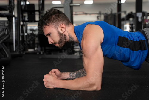Handsome male with tattoos in his 20s doing plank in the gym