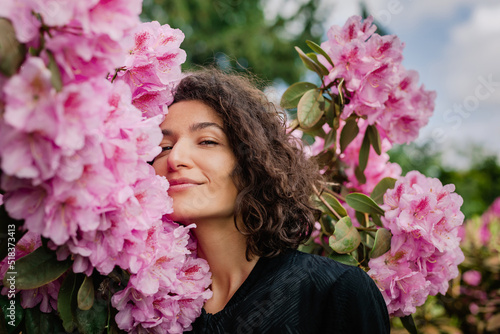 Portrait of a curly woman in pink rhododendrons looking at camera photo