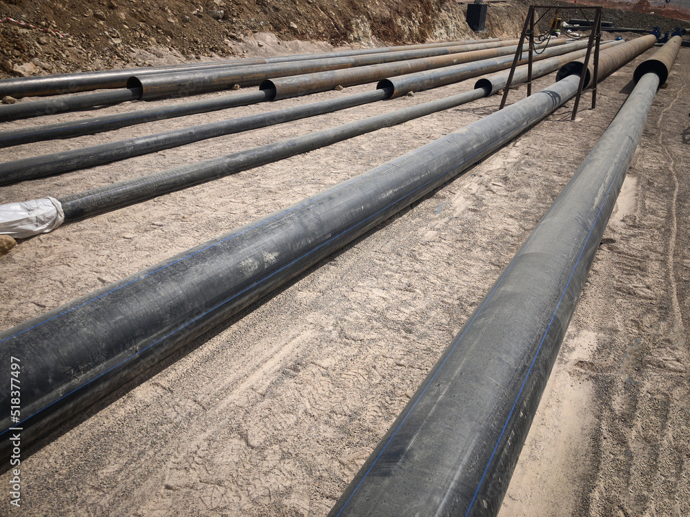 Black plastic water pipes. Industrial pipeline laid on sand foundation at construction site. 