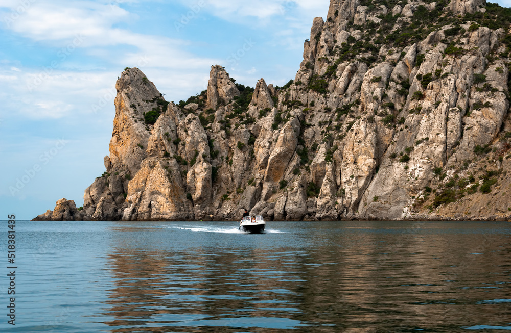 Mountain range jutting out into the sea. Mountain rock in the Black Sea. A boat with people floats on the sea.