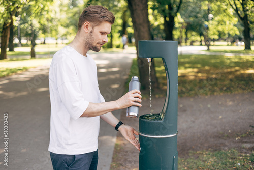 Man refilling his water bottle at the city. Free public water bottle refill station. Sustainable and green city. Heat wave. Tap water to reduce plastic bottle usage. Drinking water dispenser photo