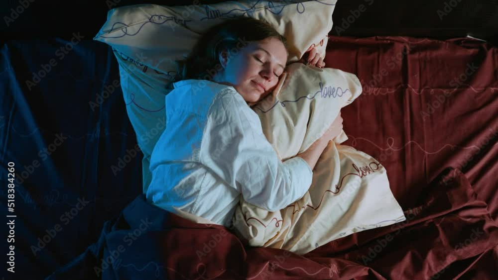The girl sleeps at night hugging a pillow. A woman smiles in a dream. The female has good dreams. Gentle, pleasant, soft bed linen. Pleasure and feeling of comfort. View from above.
