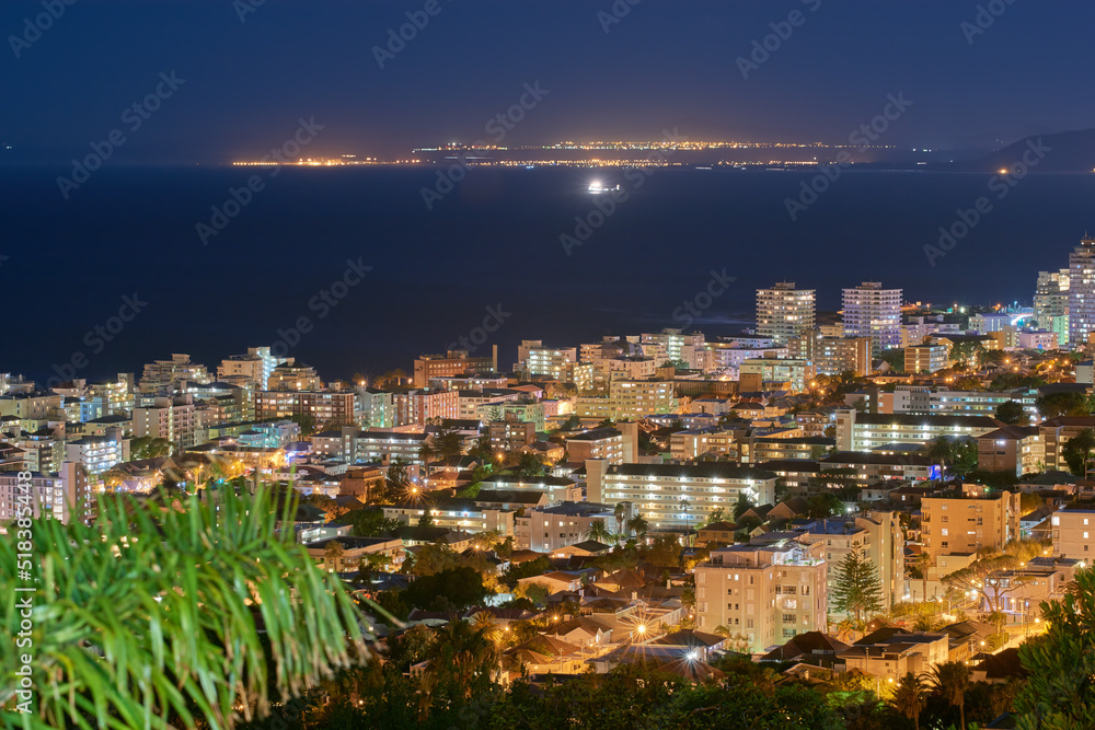 Fototapeta premium Urban city lights against a midnight sky with copy space. Skyline with colorful lighting and the open ocean on the horizon. Modern architectural buildings, vacation hotels in an urban city