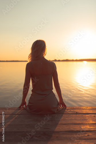 The girl sits with her back on a wooden bridge in the sunset rays