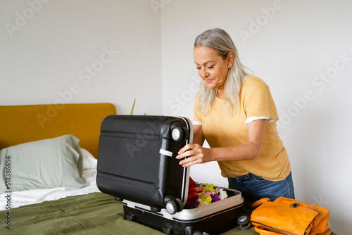 Senior woman closing suitcase on bed photo