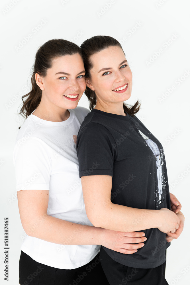 Two beautiful women twin sisters posing white background, hugging and looking at camera Two beautiful women twin sisters posing white background, hugging and looking at camera