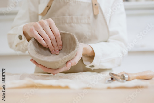 woman ceramist in the workshop makes mugs out of clay. a small business or hobby is the creation of ceramic products. an oriental young woman ceramist makes dishes and vases out of clay. handmade photo