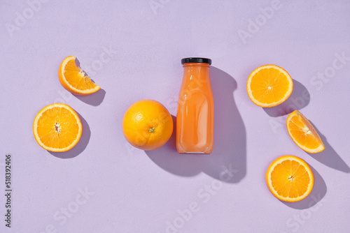 Orange juice in bottles and oranges isolated on lilac color background photo