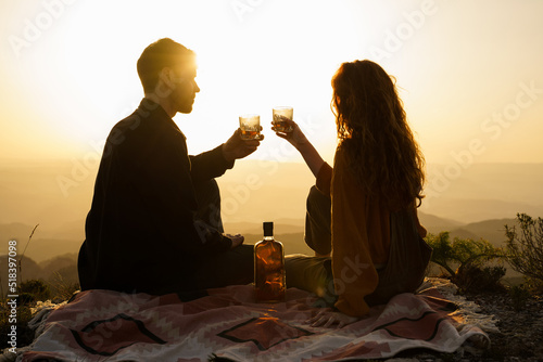 Cute couple having a drink making a toast on top of mountain at sunset photo