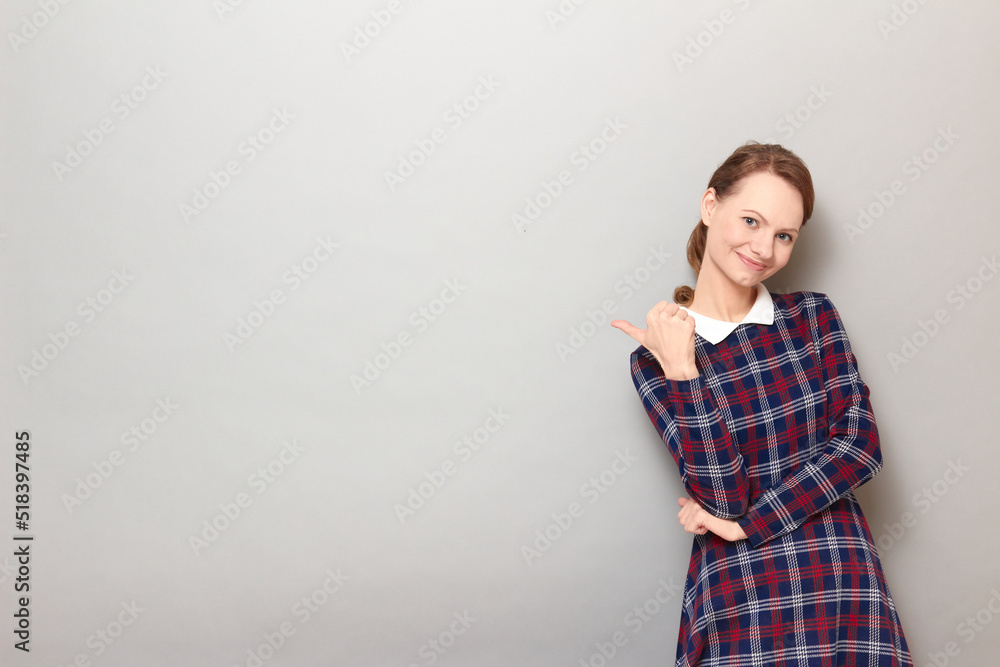 Happy young woman is pointing with thumb at copy space and smiling Happy young woman is pointing with thumb at copy space and smiling