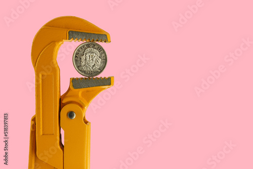 three Cuban peso coin held in an orange plumber wrench on a pink background