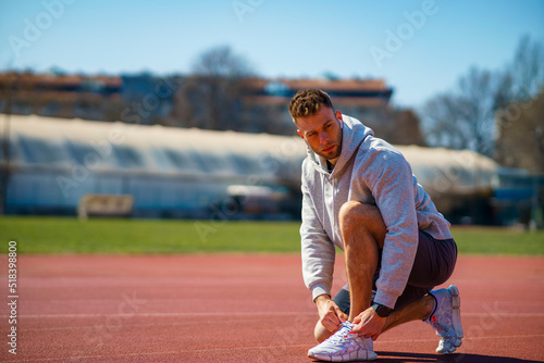Runner man tying shoelace in the stadium, cross training workout. Sporty male training outside © DusanJelicic