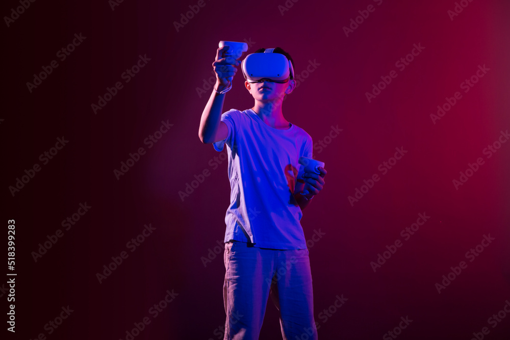 Video Gaming Concept. teenager boy playing with virtual reality goggles, VR headset, modern technology glasses with neon light on a colored background Video Gaming Concept. teenager boy playing with virtual reality goggles, VR headset, modern technology glasses with neon light on a colored background