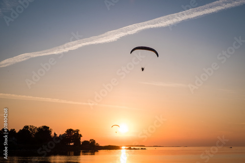 Two paraglider pilots fly in the sky during sunset on beautiful beach. Paraplanes silhouettes. Adventure vacation and travel concept.